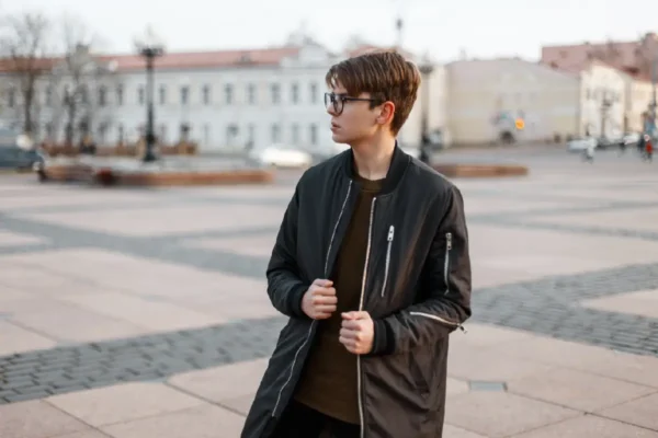 Okulary dla nastolatków, modnie ubrany nastoletni chłopak na placu miejskim w okularach